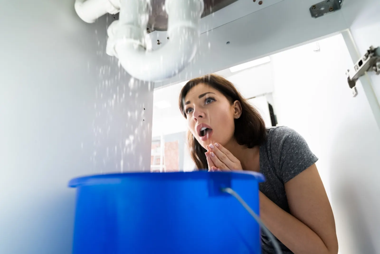 Fuite d'eau sous un évier recueillie dans un seau bleu