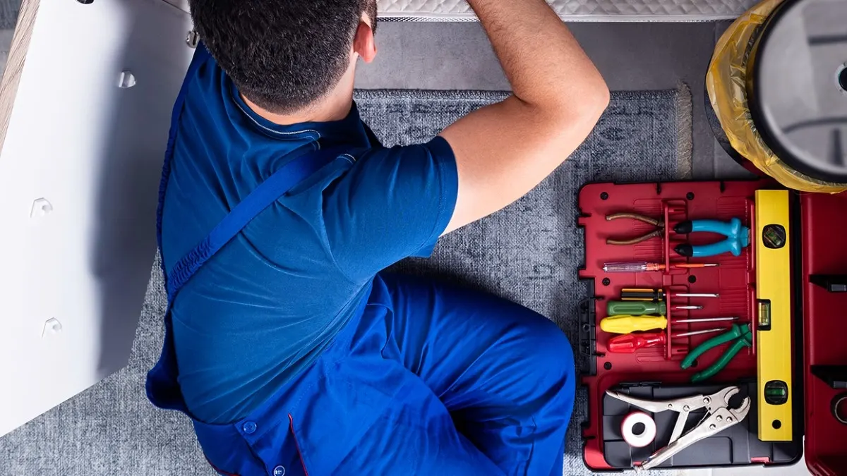 Plombier au travail sous un évier, à côté de sa mallette d'outils